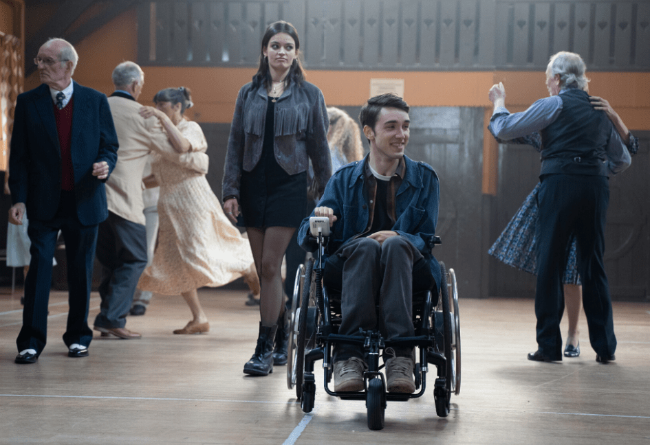 A still from Sex Education - showing Isaac and the female lead in a church hall surrounded by older couples dancing.