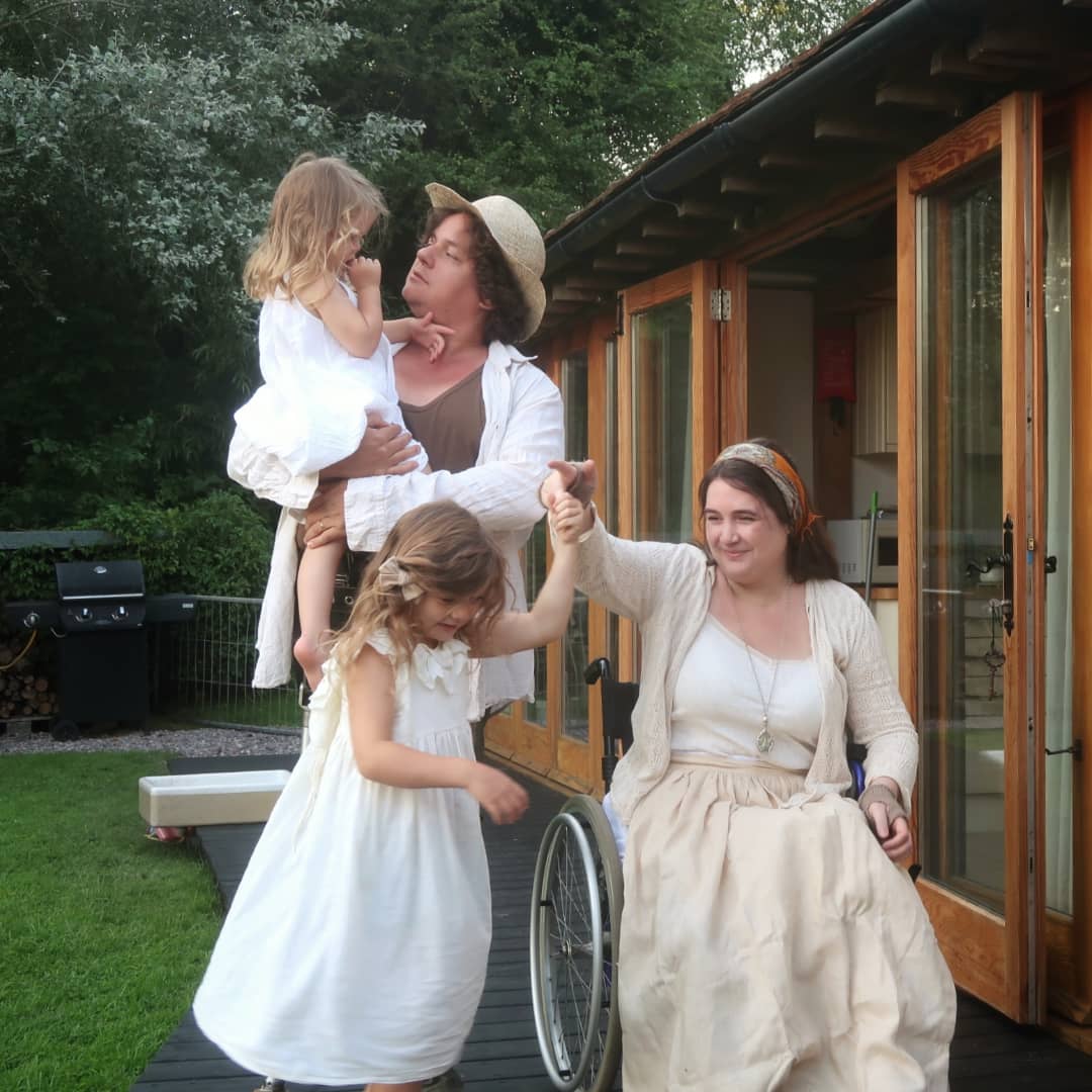 James, Lucy and their daughters - James and Lucy are disabled, Lucy's sitting in her wheelchair, twirling Mainie age 5. James is holding Viola.