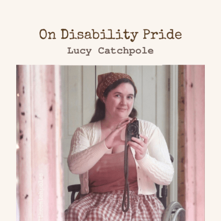 A mirror selfie. I'm a white woman wearing a brown cotton hair scarf, holding a camera and looking into the lens smiling. The words "disability pride..." are written at the top with a cream torn paper background. The mirror frame is very old and cracked, and is cream, though it looks mysteriously pinkish here.