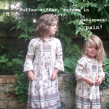 Viola (2) and Mainie (6) are standing next to each other in front of a wonky raised flower bed full of jasmine. They're both white with light brown blondish hair. They're wearing matching long floral dresses - a 70s festival vibe. Mainie looks very serious about the song, a dark rewrite of Twinkle Twinkle Little Star. Viola whispers the last word of each line. They both look DELIGHTED at the end and Viola rushes towards the camera.]