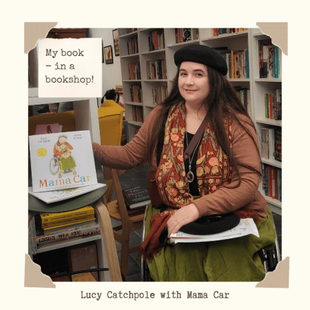 Lucy Catchpole with Mama Car in a bookshop. Lucy's in Caper Oxford next to a display of my picture book Mama Car, sitting in my wheelchair, smiling at the camera. I’m wearing my green linen skirt, burnt orange cardigan, embroidered scarf & black beret. Mama Car cover art: a white background, a wheelchair-using mother on the front with a child on her lap, who looks slightly like me - illustrated by Karen George. Text over the top reads "My book in a bookshop!" on paper. It's a bright, cosy bookshop.