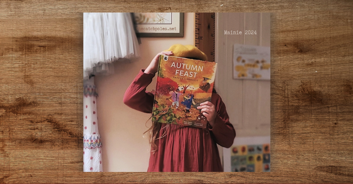 Mainie - age 9 - holds a copy of Autumn Feast: Nature’s Harvest in front of her face. It’s a beautiful illustrated picture book with lush, rich autumn colours - two children play in fallen leaves on the cover. Mainie’s wearing a russet-red dress, and mustard coloured beret. Labelled 'Mainie 2024'