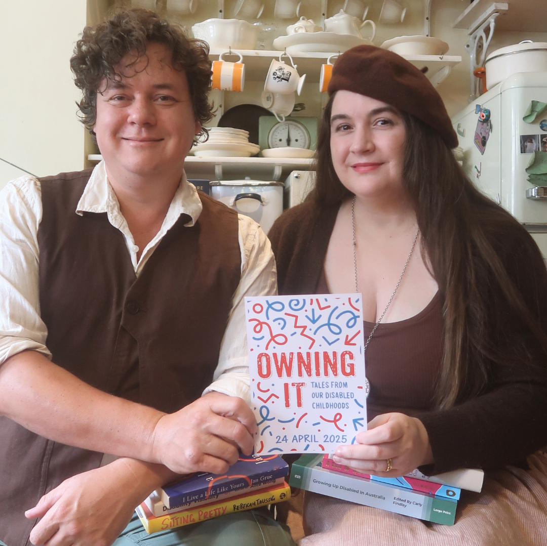 Book announcement! Lucy and James - a white disabled couple - sit in their kitchen holding a large postcard with the title ‘Owning It: Tales From Our Disabled Childhoods’. Text reads ‘Announcement!’ on cream torn paper. It’s a cosy room with teacups and crockery on shelves. James is wearing a linen shirt and the new brown waistcoat, Lucy is wearing a dark brown cardigan and matching beret - we’re both smiling. We’re holding books by some of the contributors.